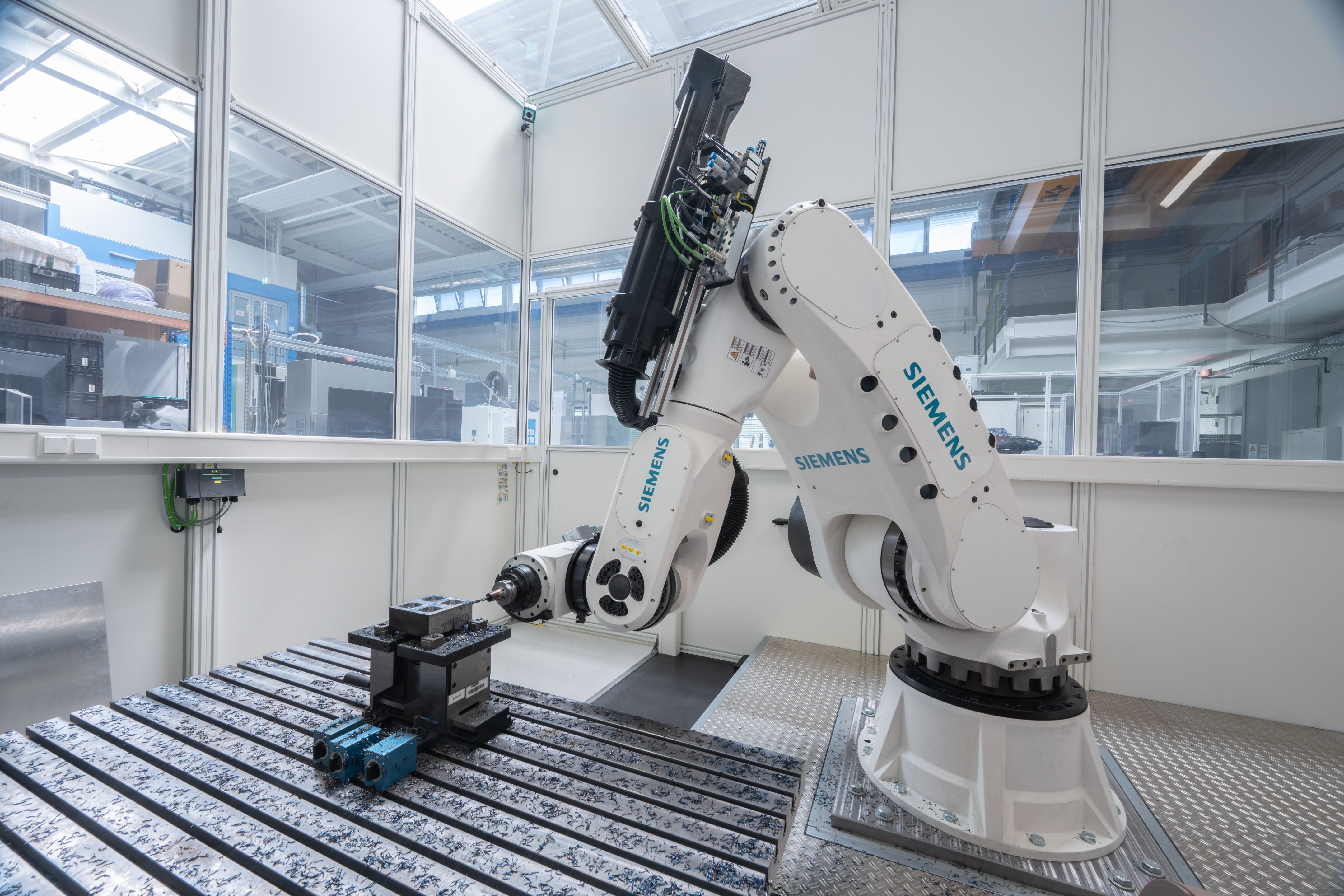 A multi-axis robot bearing the Siemens logo is machining a steel workpiece