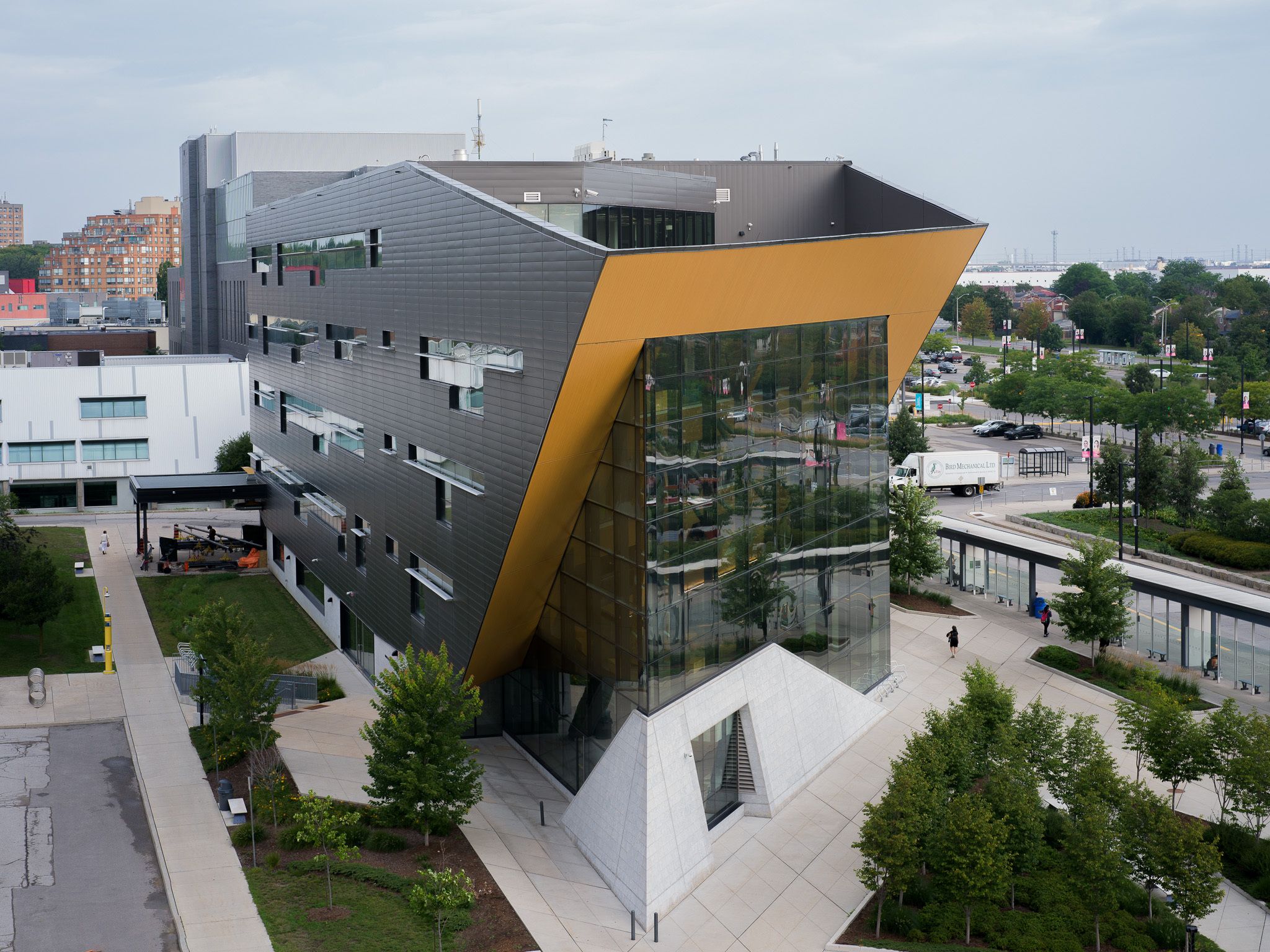 Modern angular building with dark metal cladding, a large glass facade, and bold yellow architectural accents.