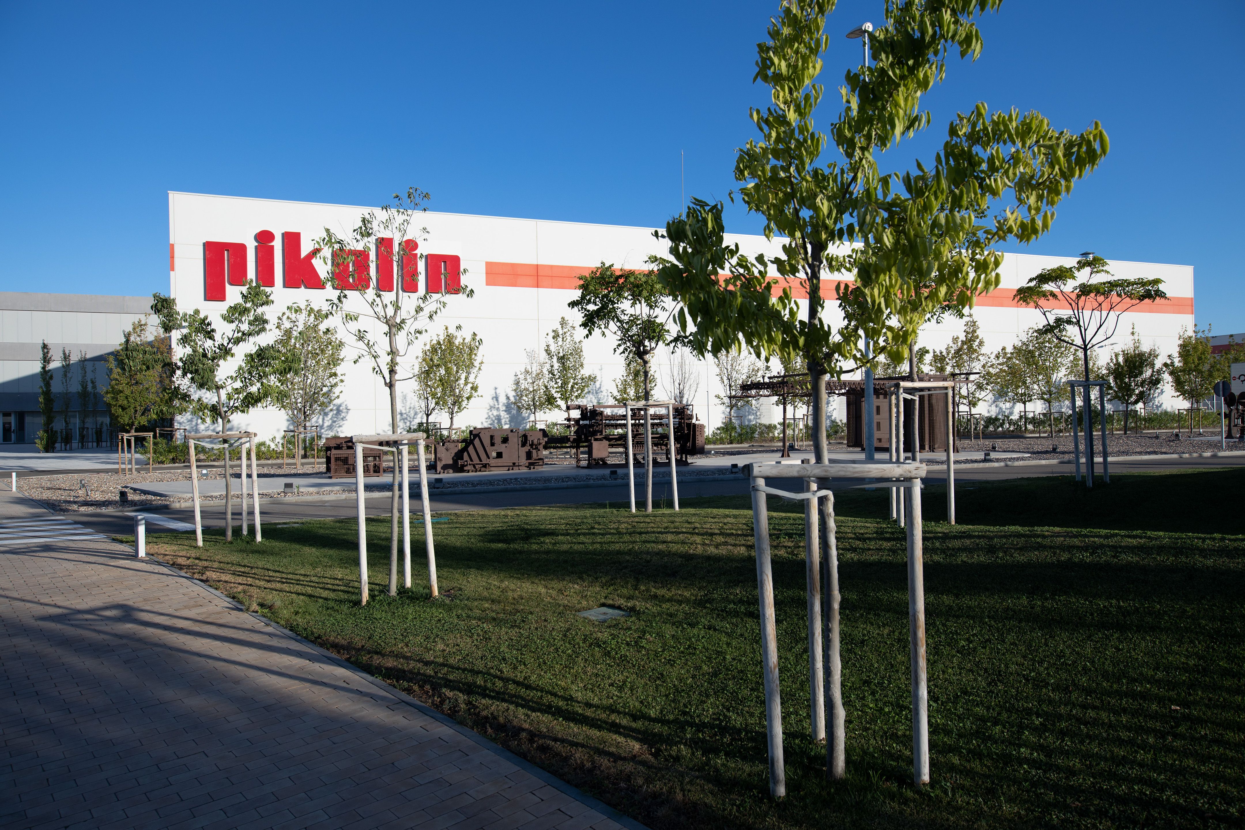 An exterior shot of a factory building, with “Pikolin” printed in red on the side of the building and trees in front of it.