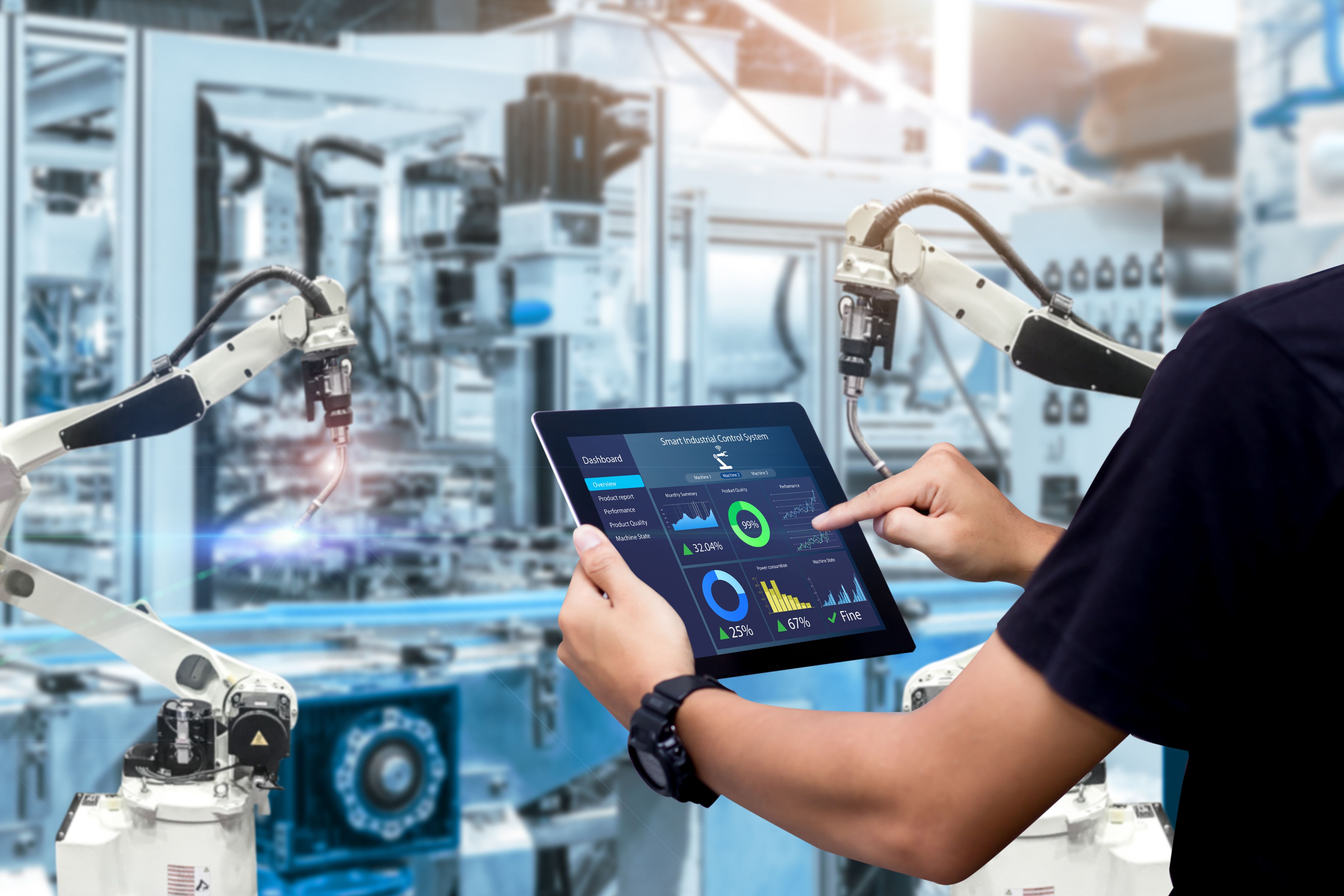 Person pointing on a tablet beside robotic arms in an automated manufacturing facility.