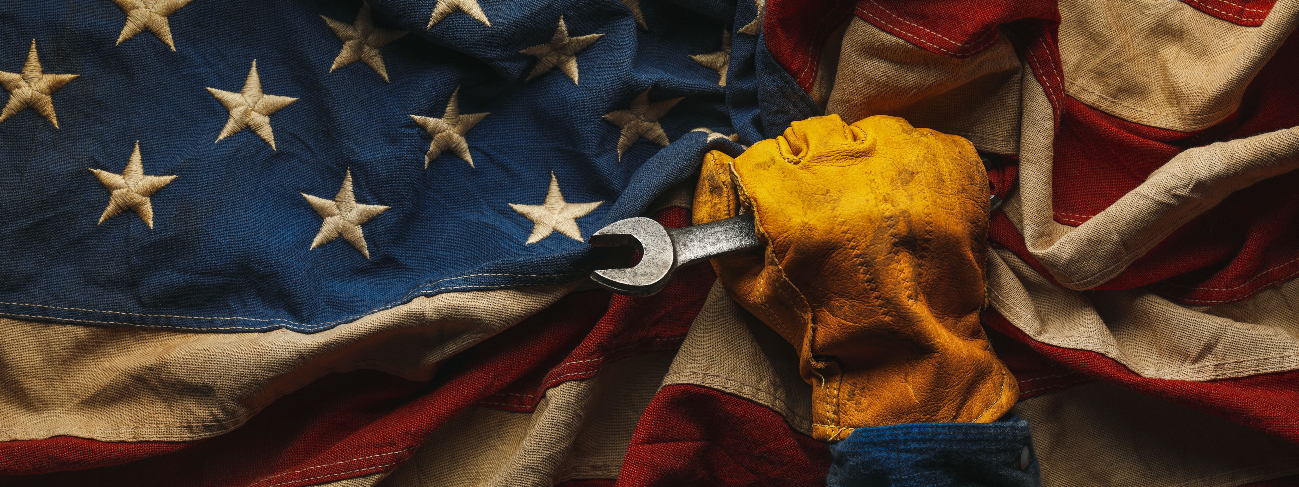 A hand wearing a work glove holding a wrench resting on the American flag.
