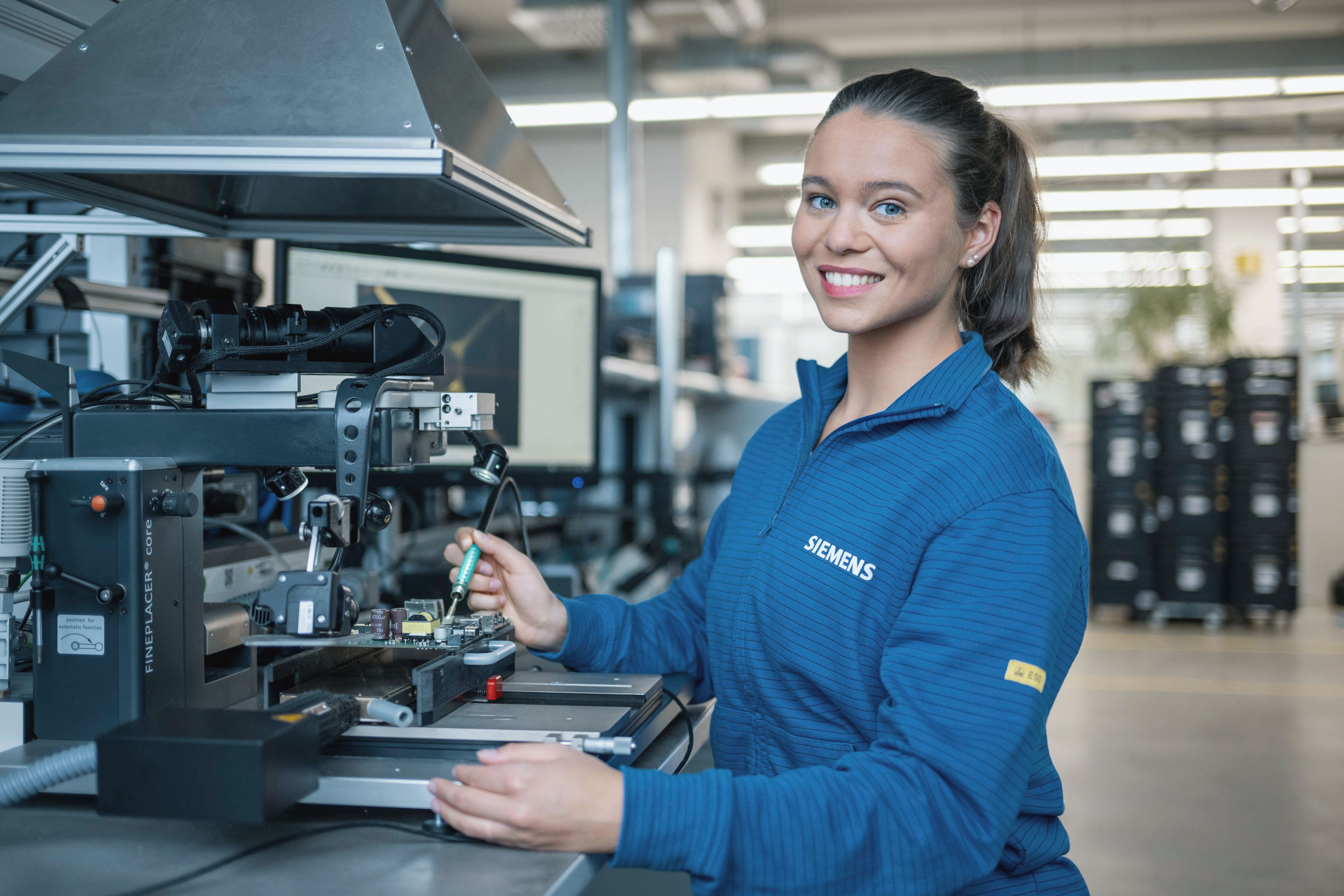 Person i blå Siemens-skjorte, der betjener industriel maskine i et værksted