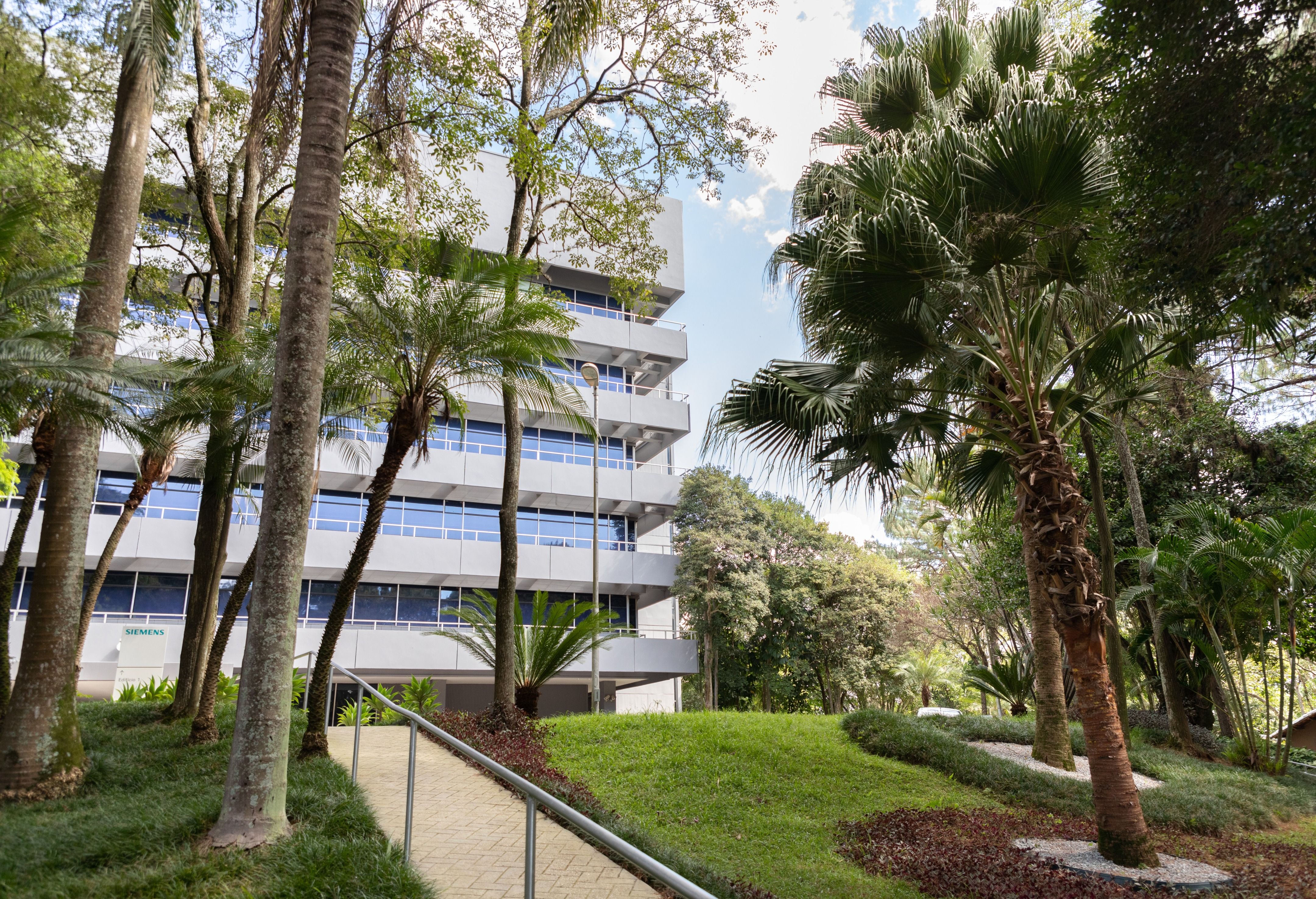 Modern multi-story building surrounded by palm trees, landscaped lawn, and a winding garden path.