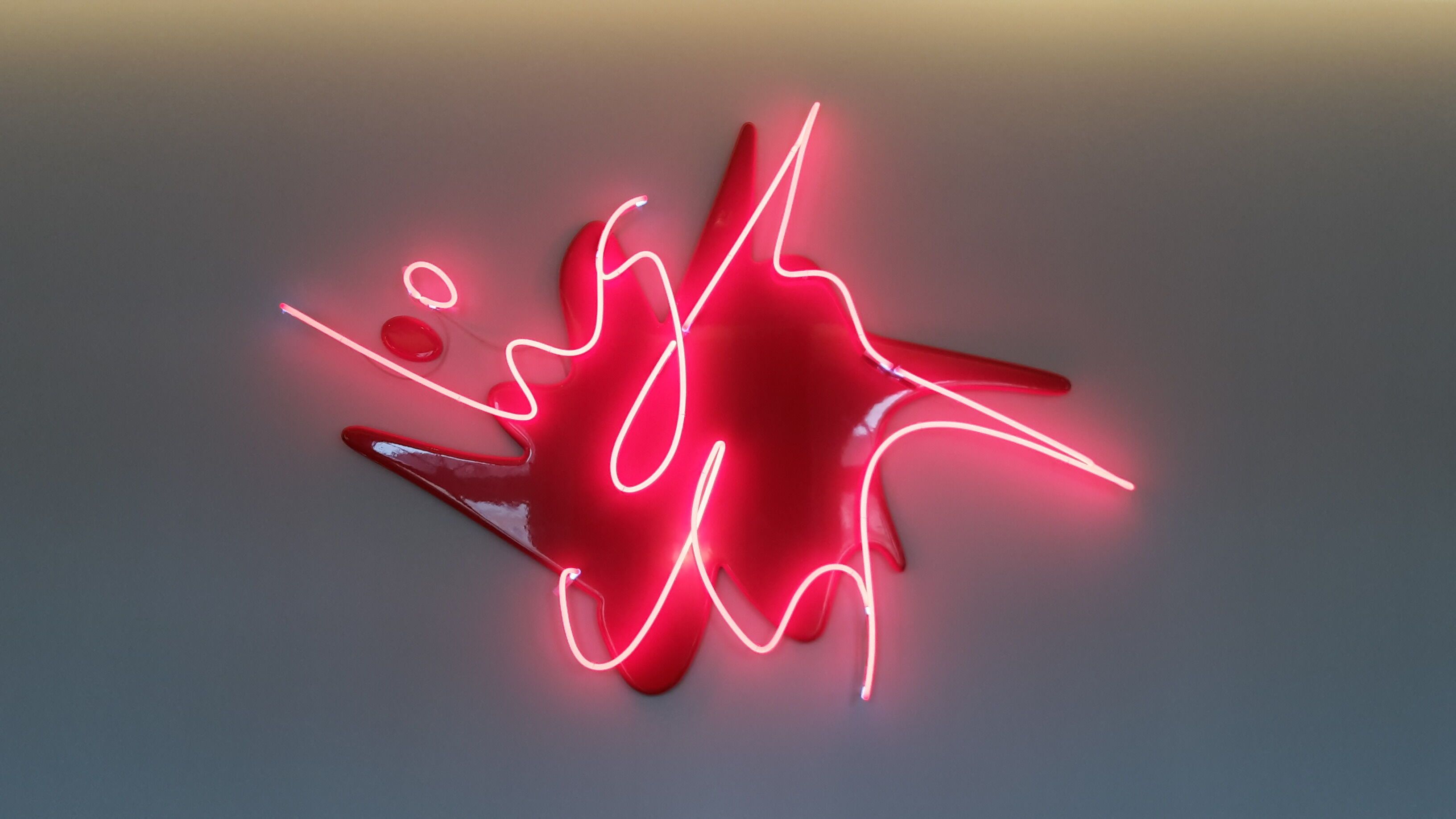 Abstract red wall sculpture with glowing pink neon lines looping across a red angular shape.