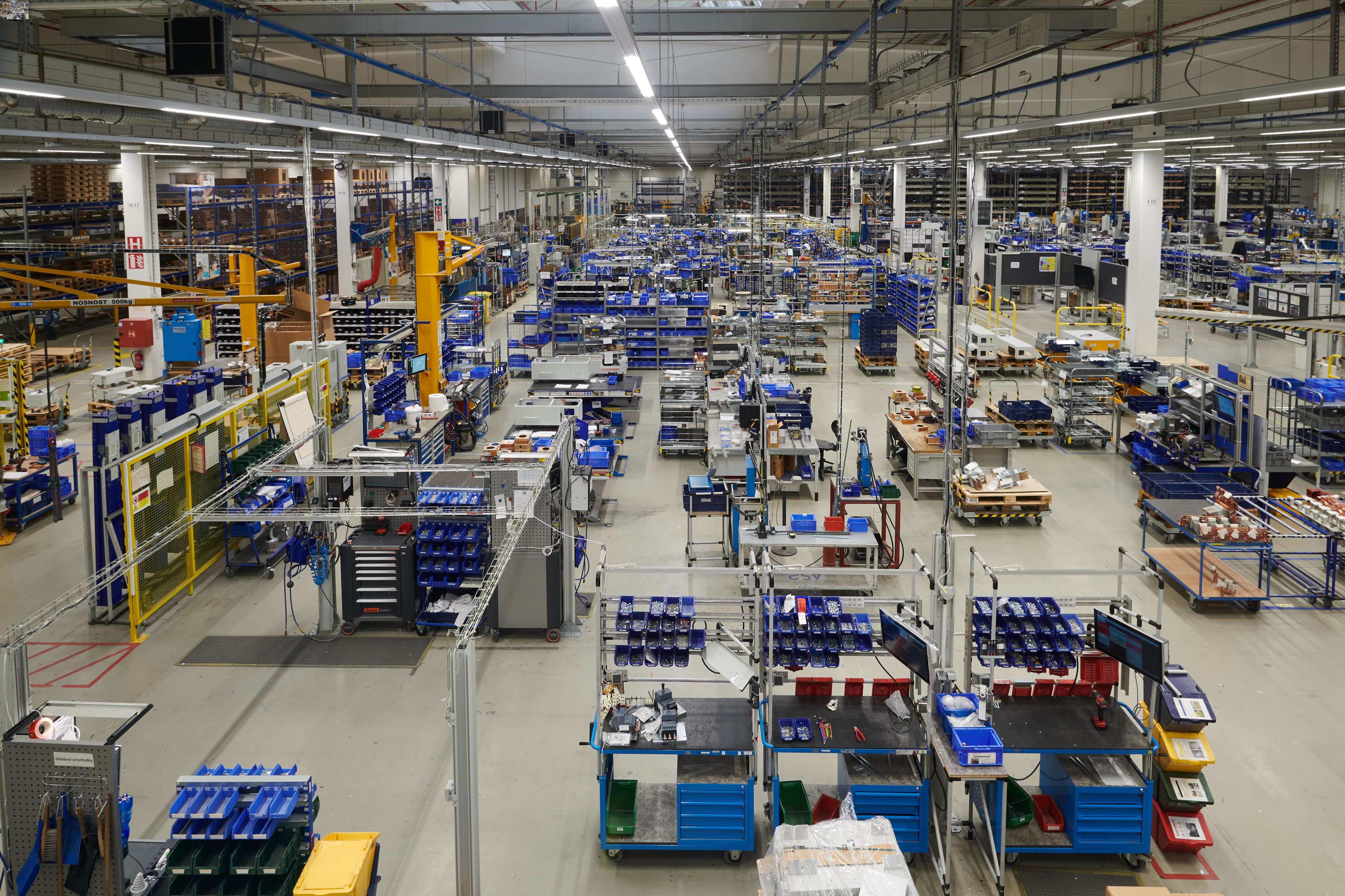 A wide-angle view of a bright, organized industrial warehouse with workstations, assembly benches and storage racks