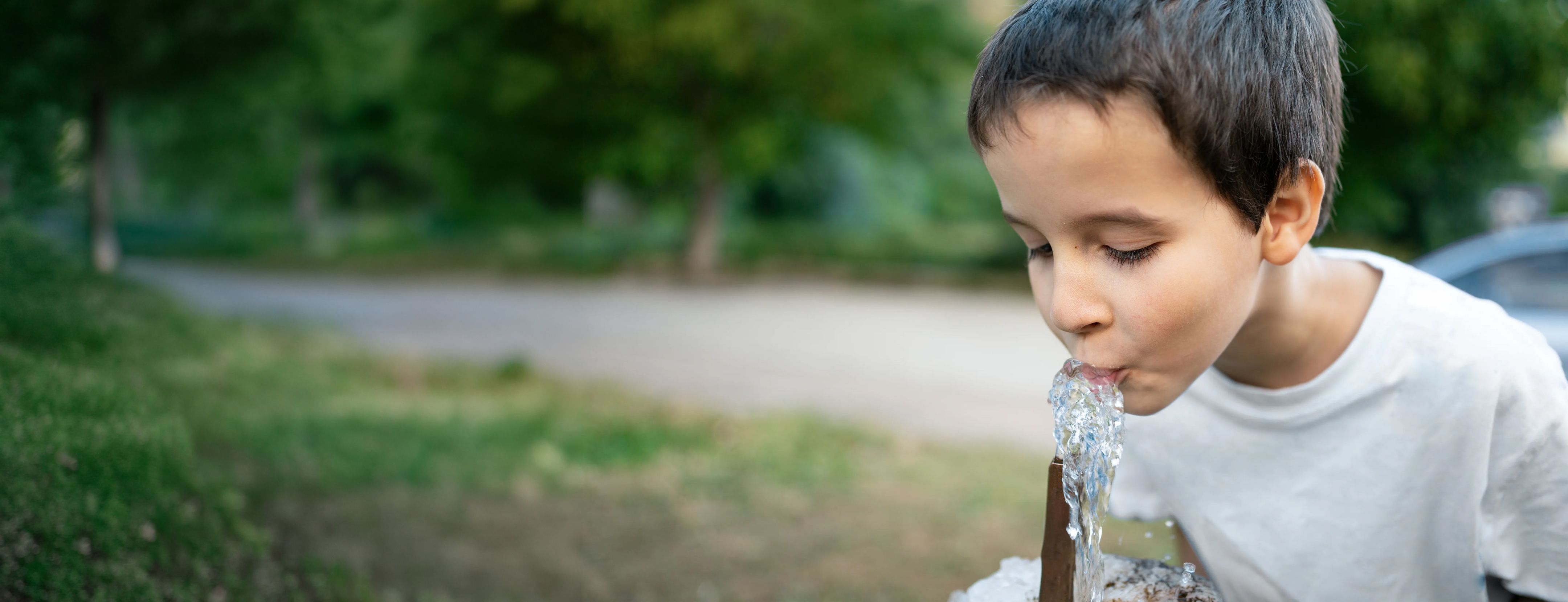 Child drinking water from cupped hands, smiling, with water droplets splashing around