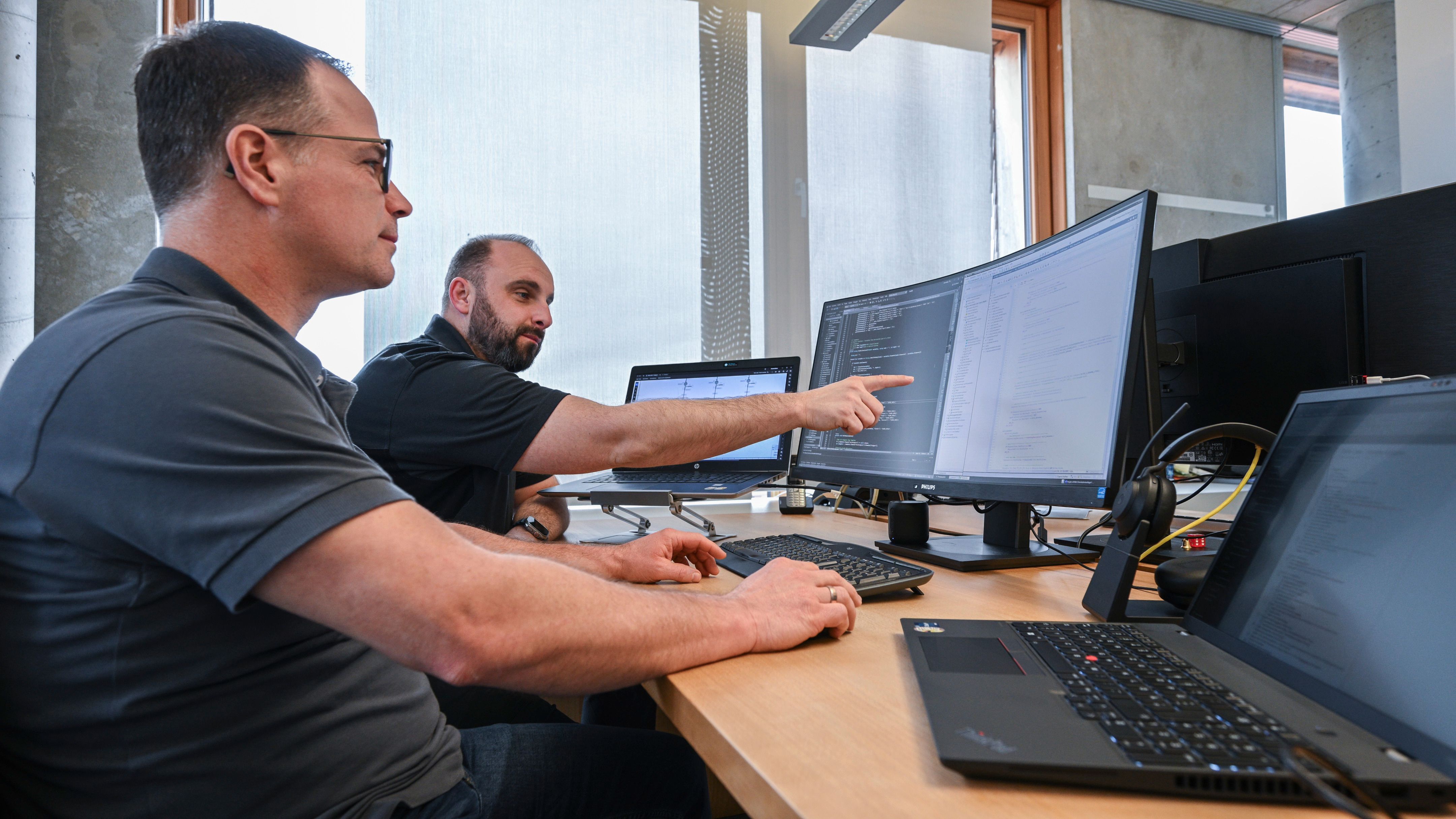 Two engineers reviewing PLC code on multiple monitors.