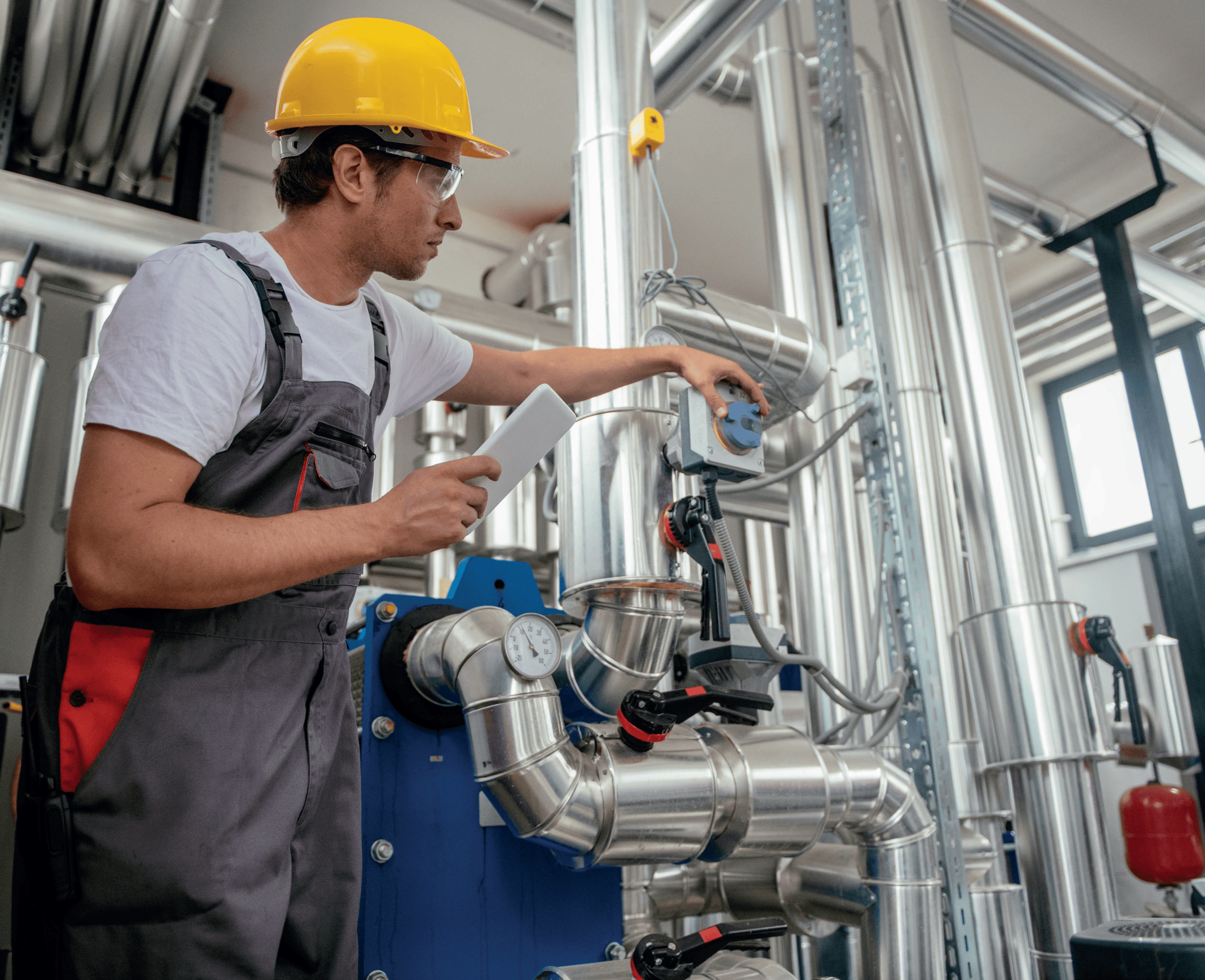 Technician in safety gear inspecting industrial piping equipment.