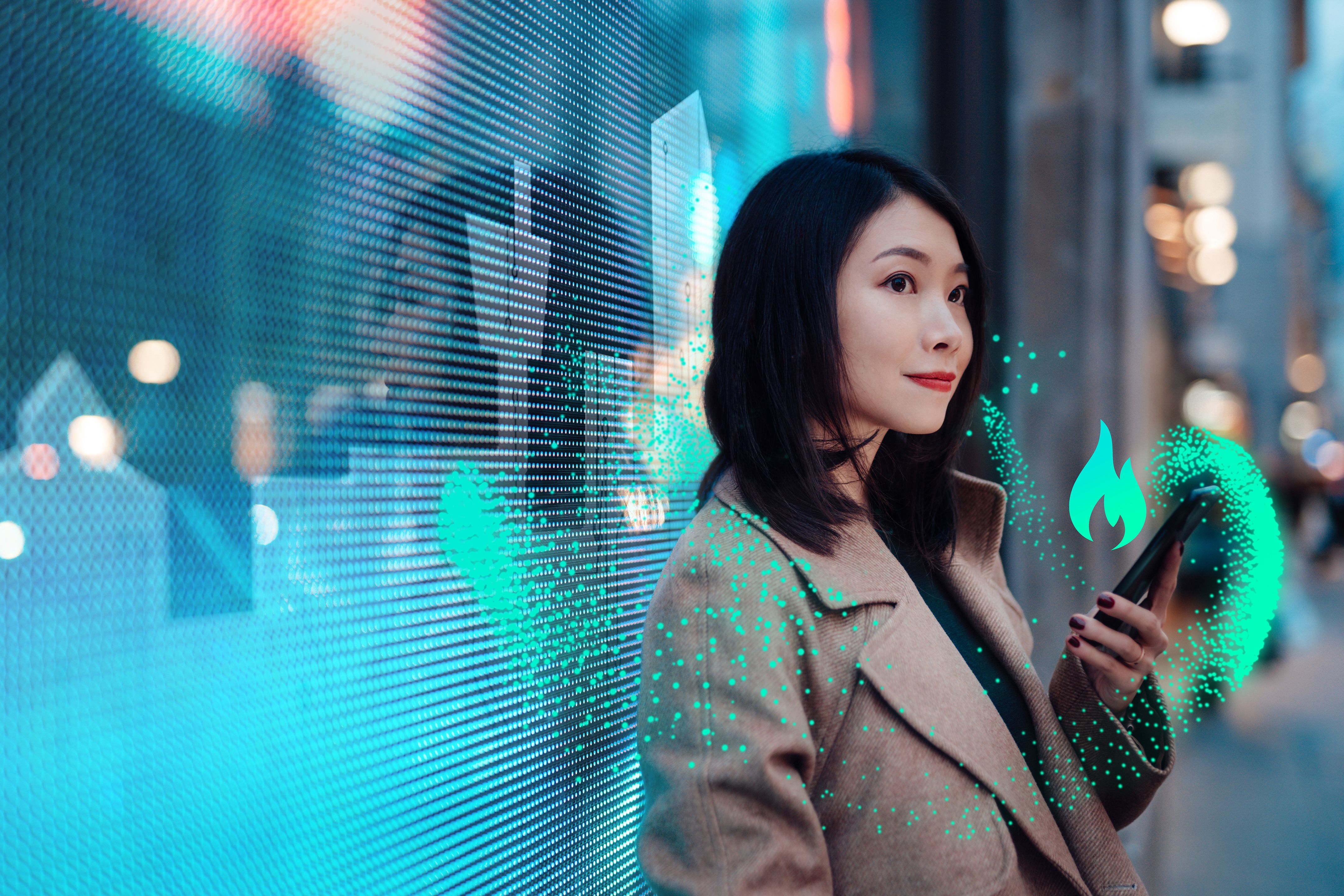A woman in a coat holds a phone with a digital flame icon and green particles, standing by a blue digital display.