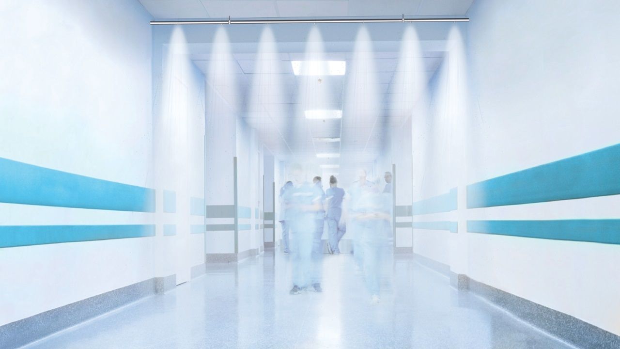 A long, bright hospital corridor with blurred figures of medical staff and a water mist spray bar installed overhead.
