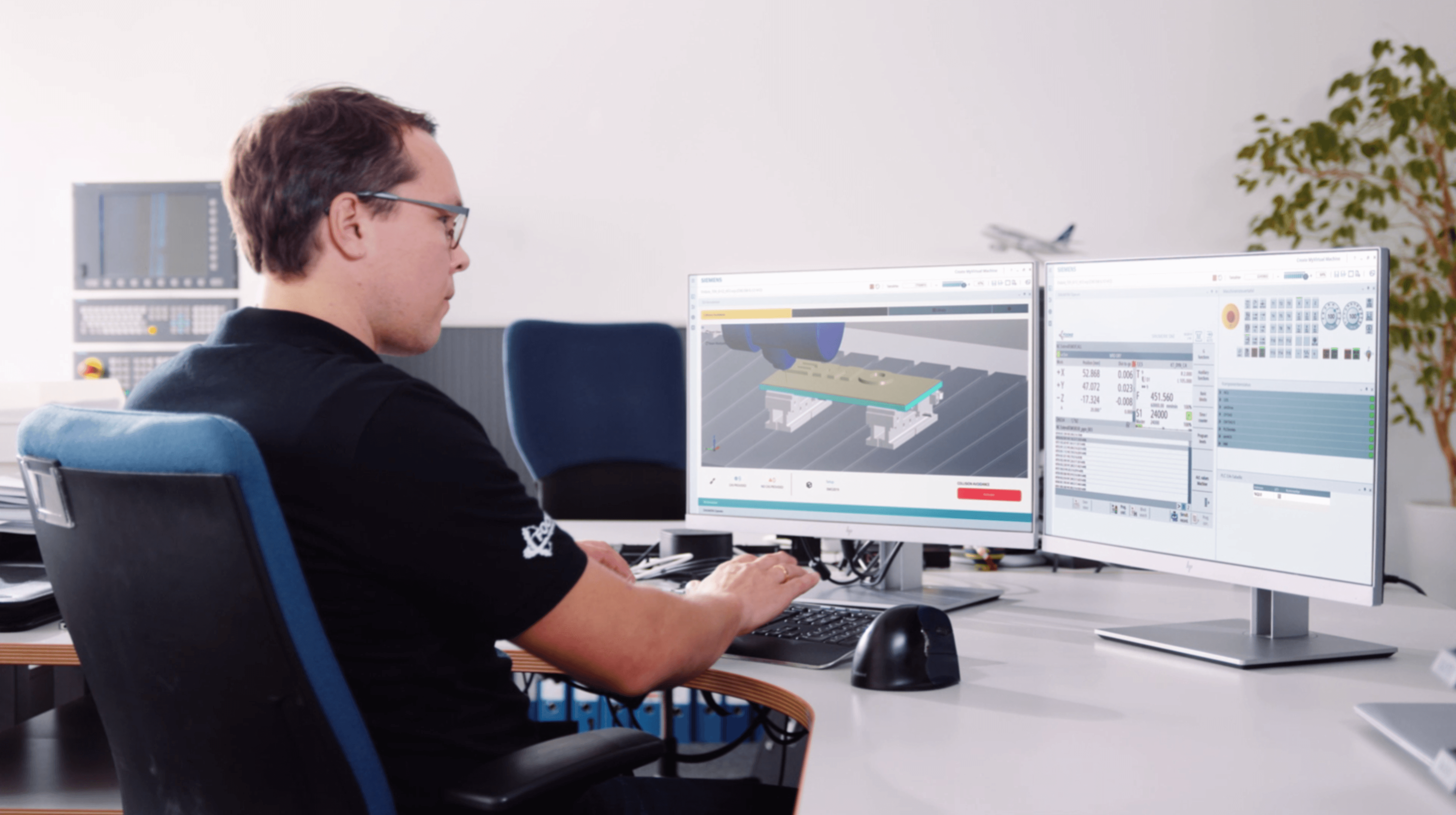 CNC operator working with a digital twin simulation on a dual-monitor workstation