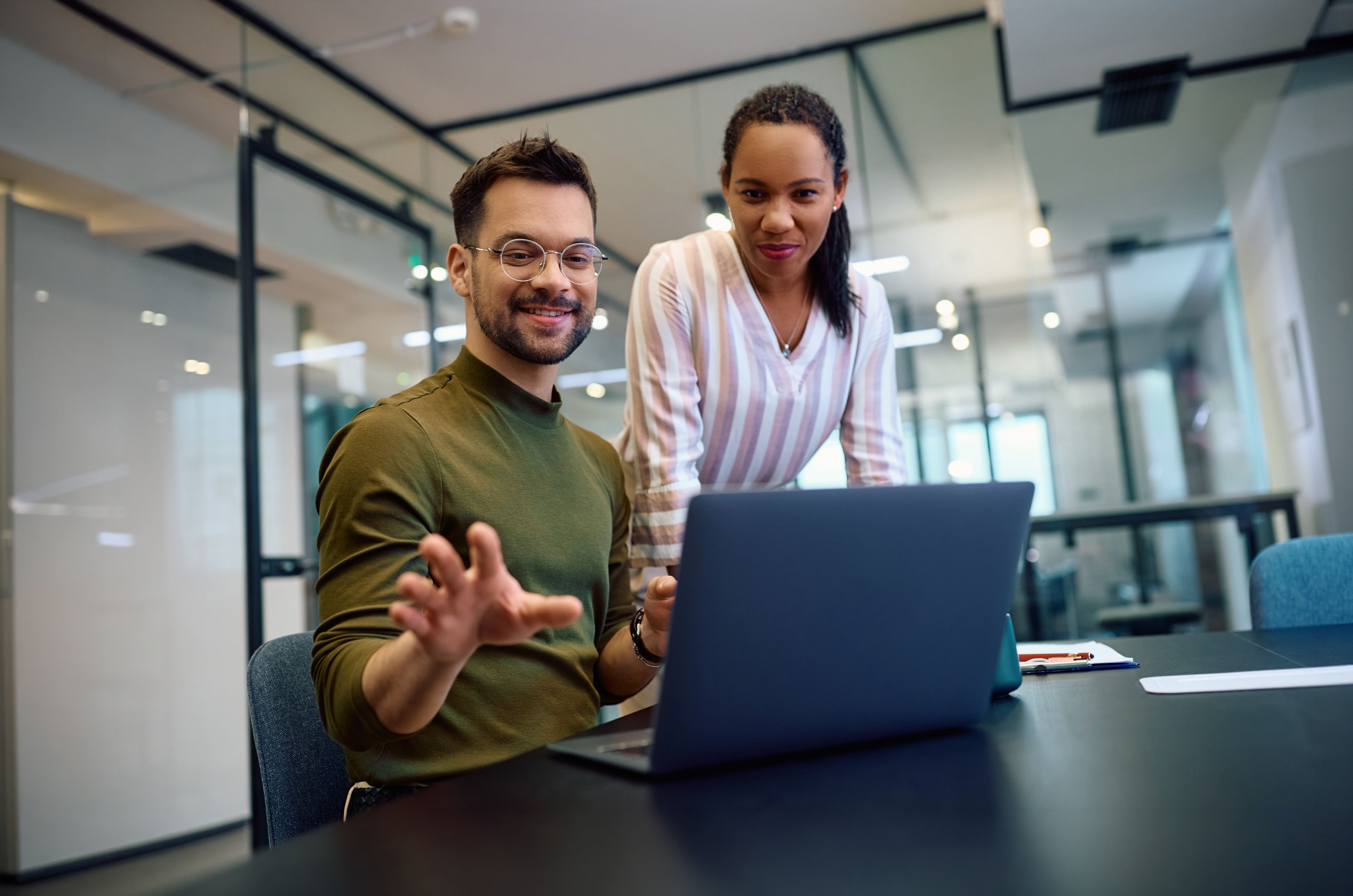 Twee collega's werken samen in een modern kantoor, kijkend naar het scherm van een laptop