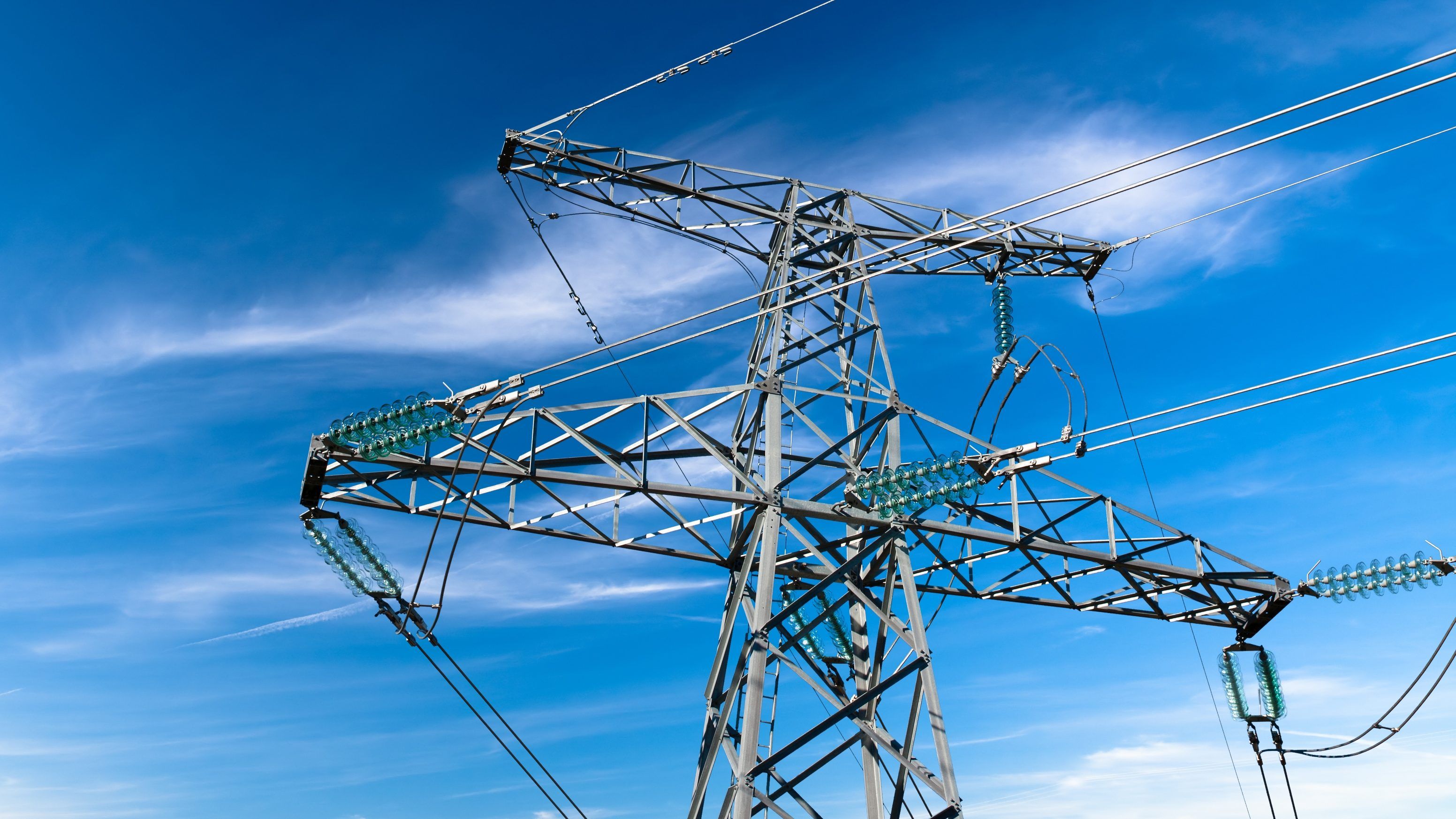 Nagyfeszültségű elektromos átviteli torony távvezetékekkel és üvegszigetelőkkel a fényes kék ég ellen felhőkkel.