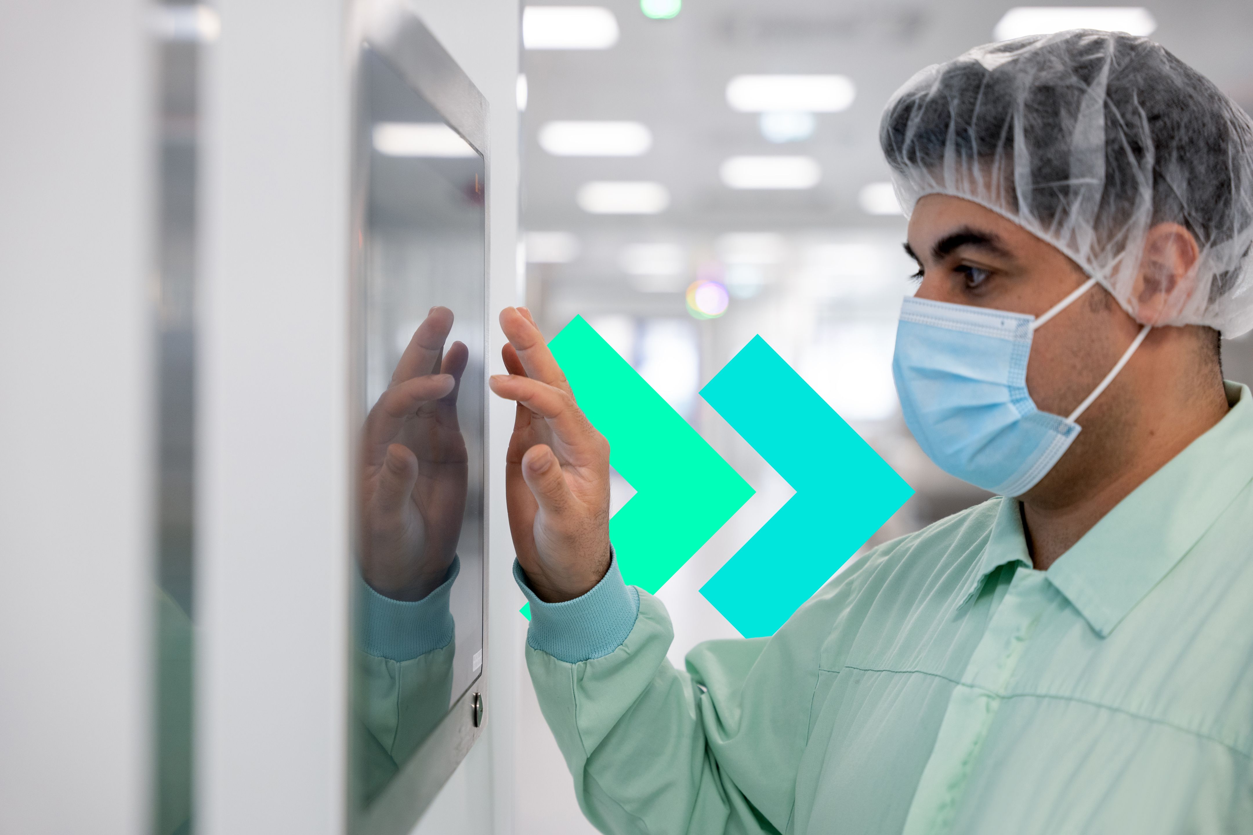 Pharmacist wearing a mask, hair cover and scrubs in a lab working on a touchscreen monitor