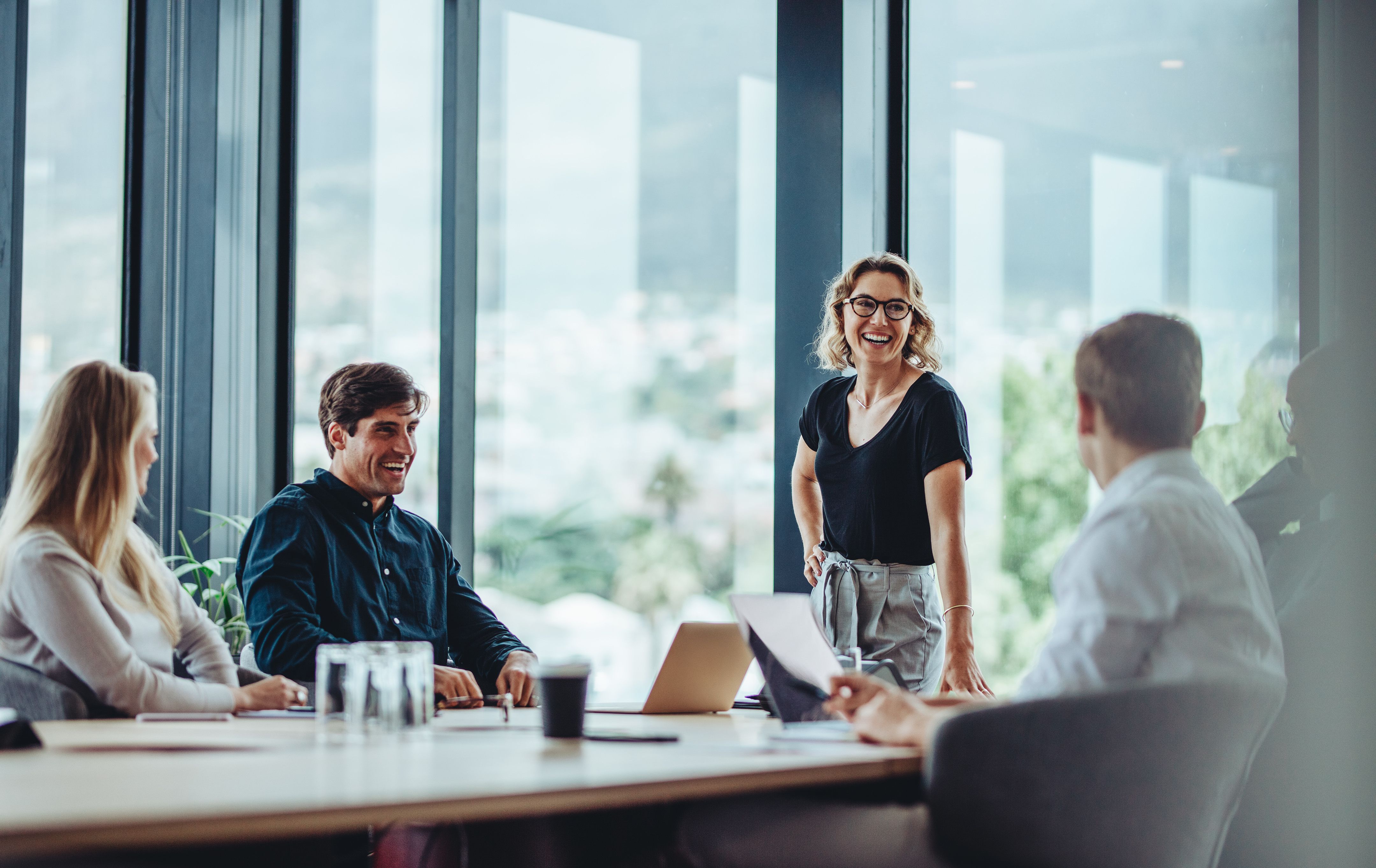 A female sales leader stands in front of a conference table leading a meeting