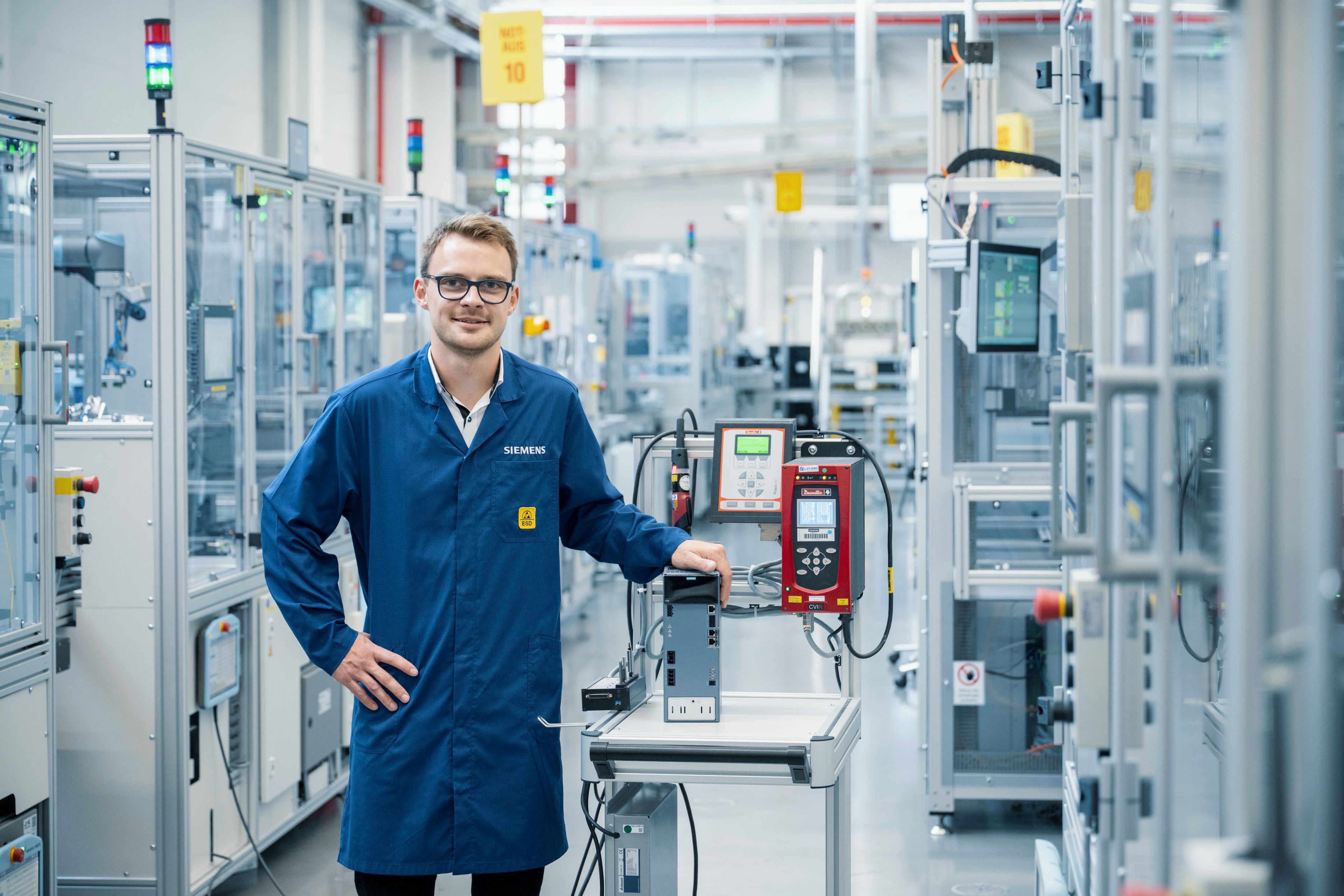 Person i Siemens laboratoriefrakke, der betjener en testenhed ved siden af et fremstillingssystem.