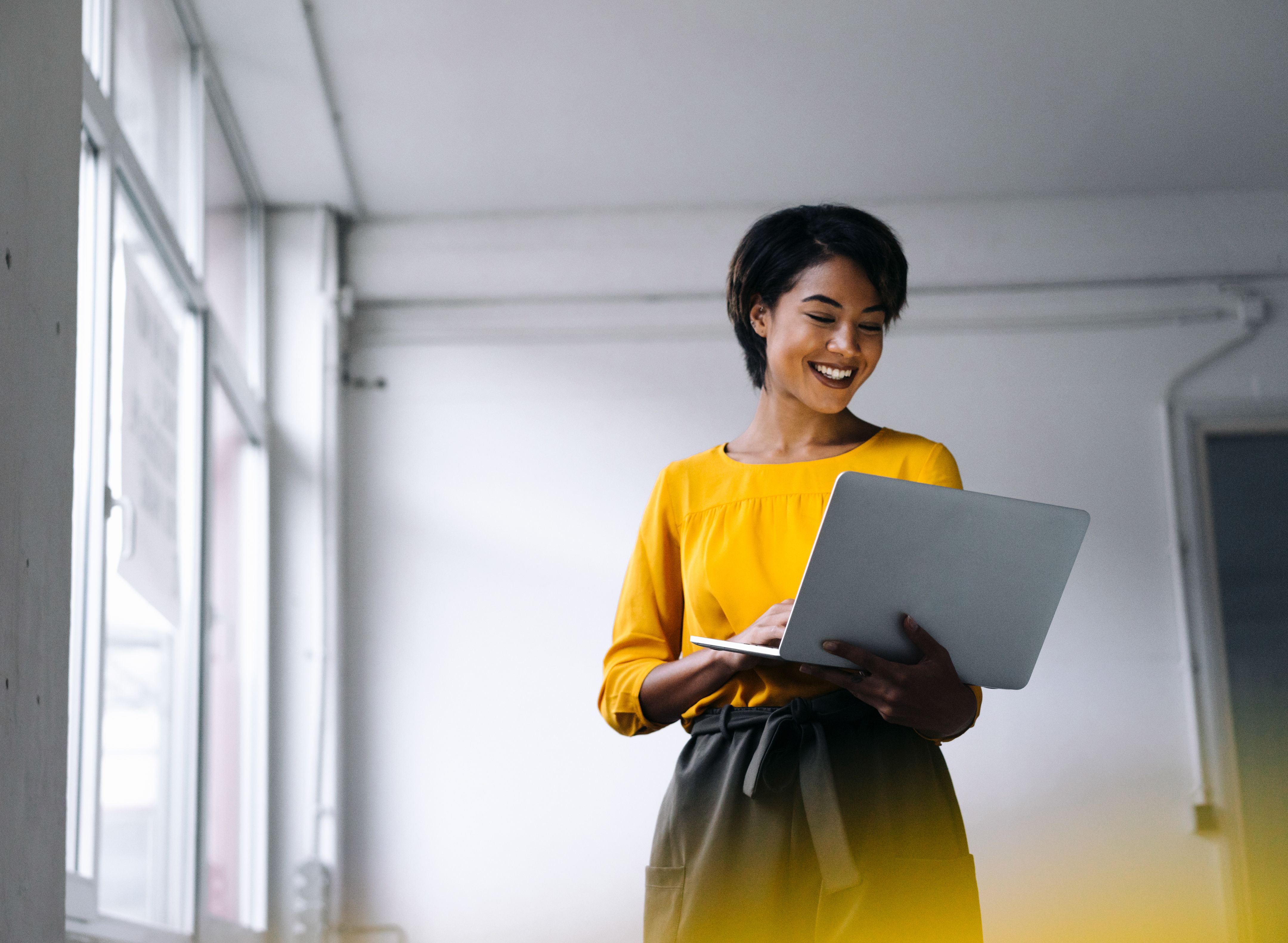 Una donna sorridente tiene un laptop aperto in un ufficio moderno.