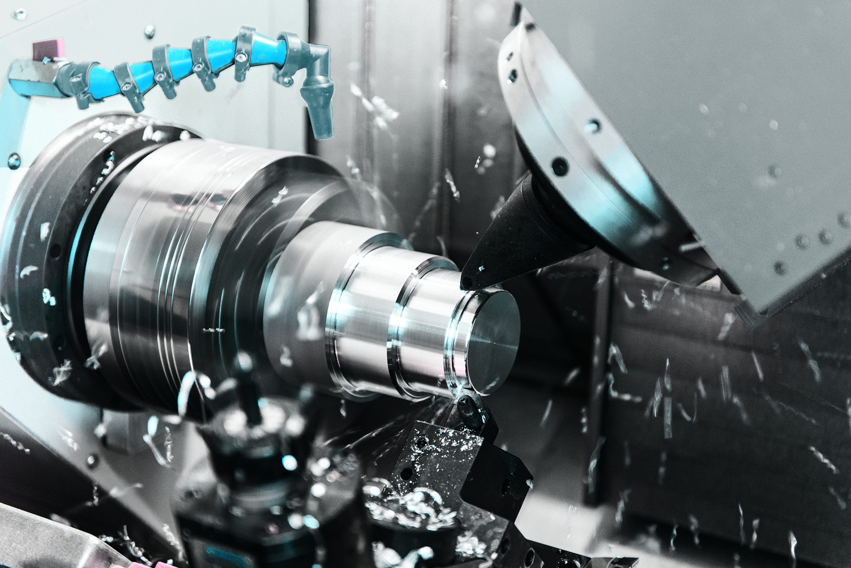 CNC lathe machining a cylindrical metal workpiece, with coolant spray and cutting tools in action