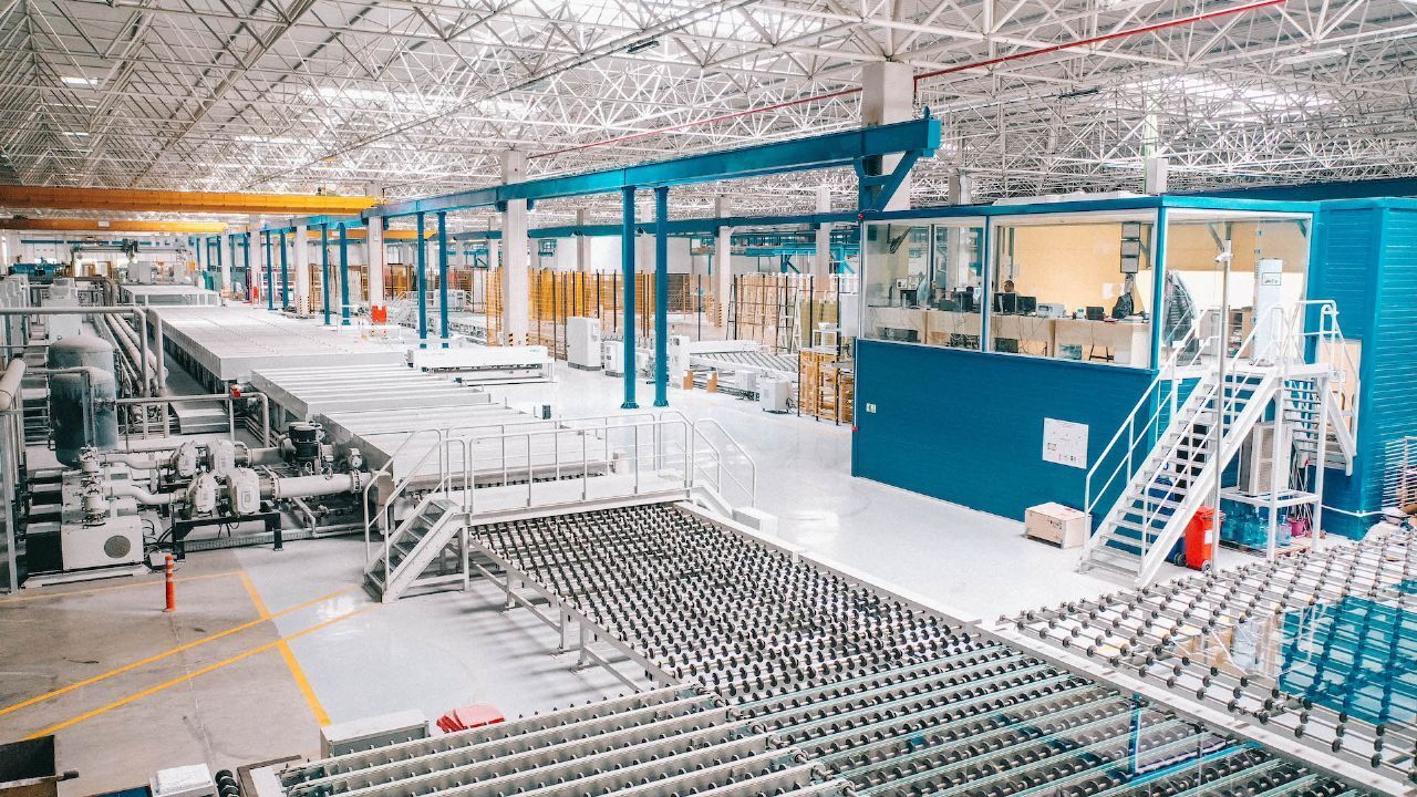 A wide shot of a modern glass manufacturing plant with conveyor belts and a control room.