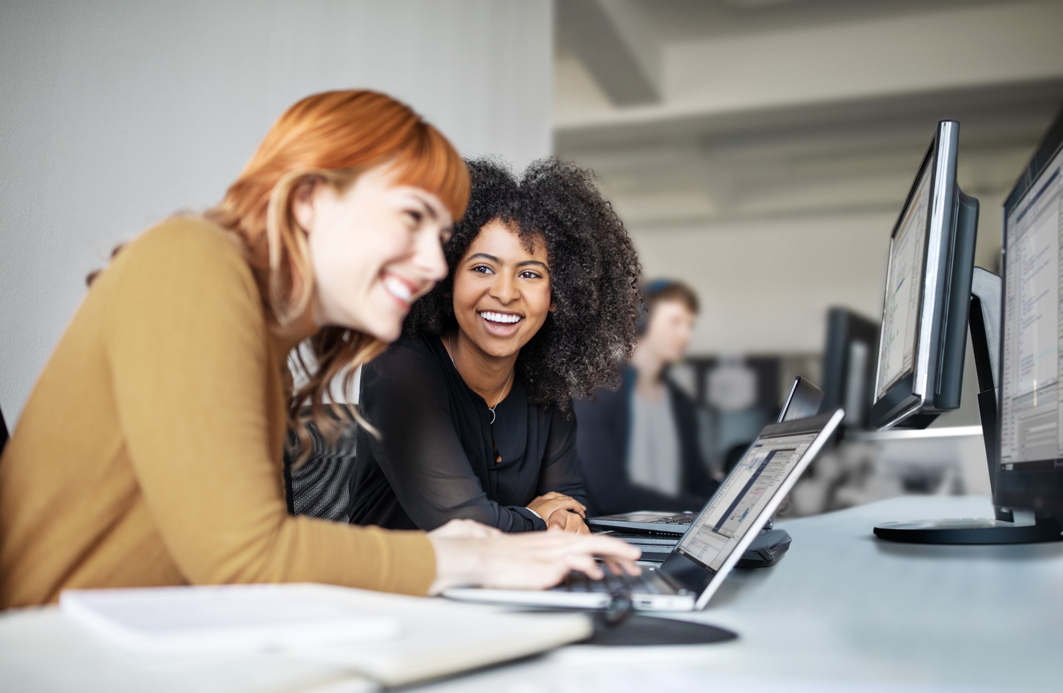 Two female coworkers look at a laptop screen and laugh together