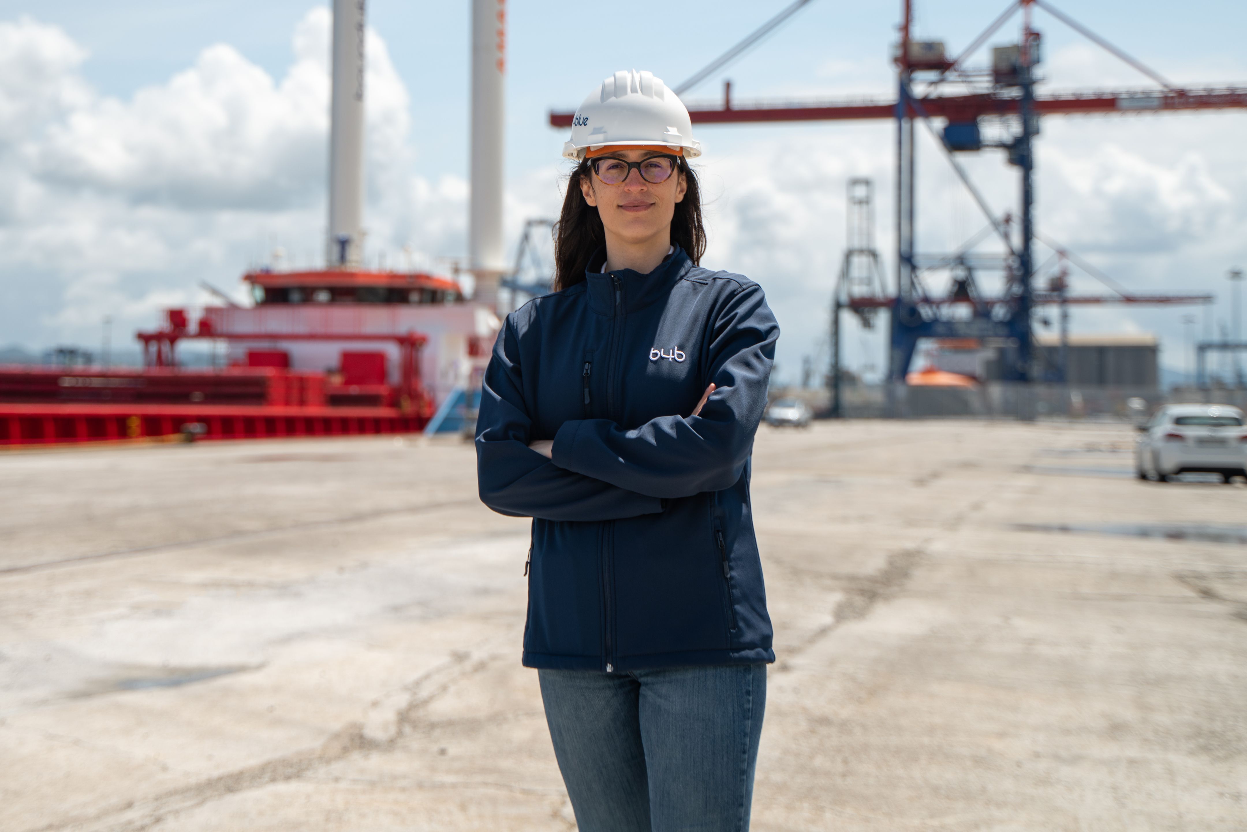 Professional in a hard hat standing at a port terminal with cargo cranes and industrial infrastructure in the background