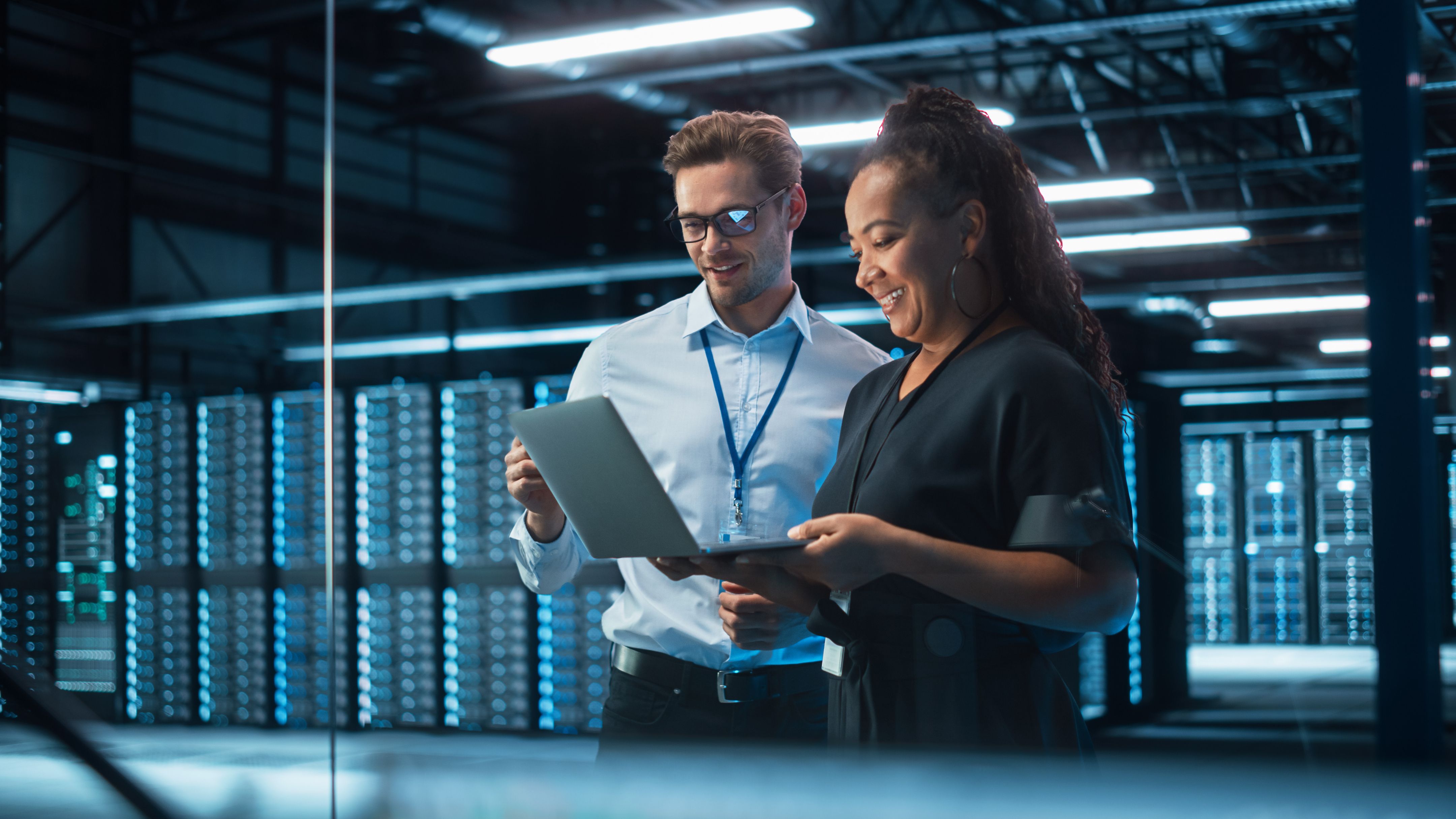  Two employees are standing in the rack room of a data center to check data in the laptop.