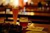 A glass of  beer next to a mug of beer on a bar top
