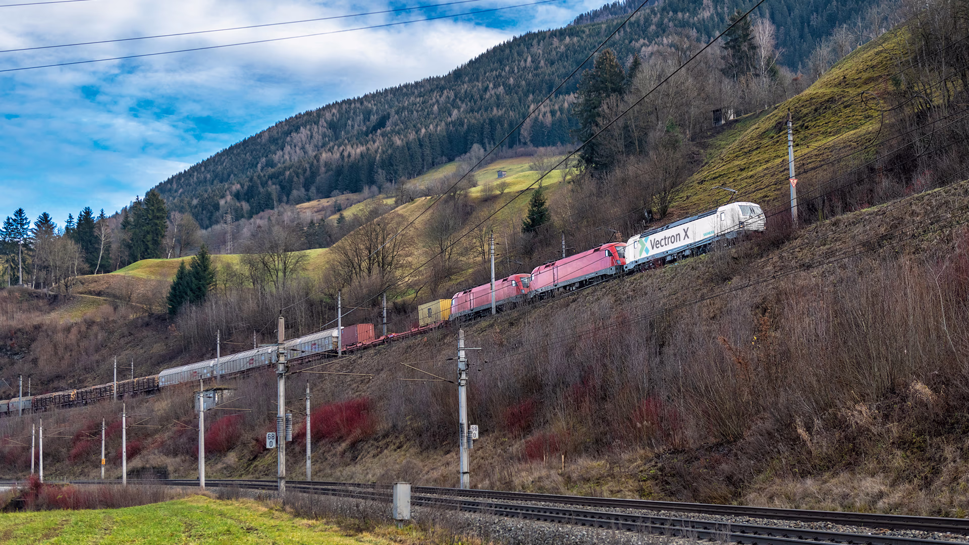 Vectron locomotive driving through the mountains, pulling a freight train and several additional locomotives behind it. Vectron locomotive driving through the mountains, pulling a freight train and several additional locomotives behind it.