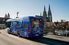 A blue public transport bus with an electric motor drives through a street in Regensburg, Germany