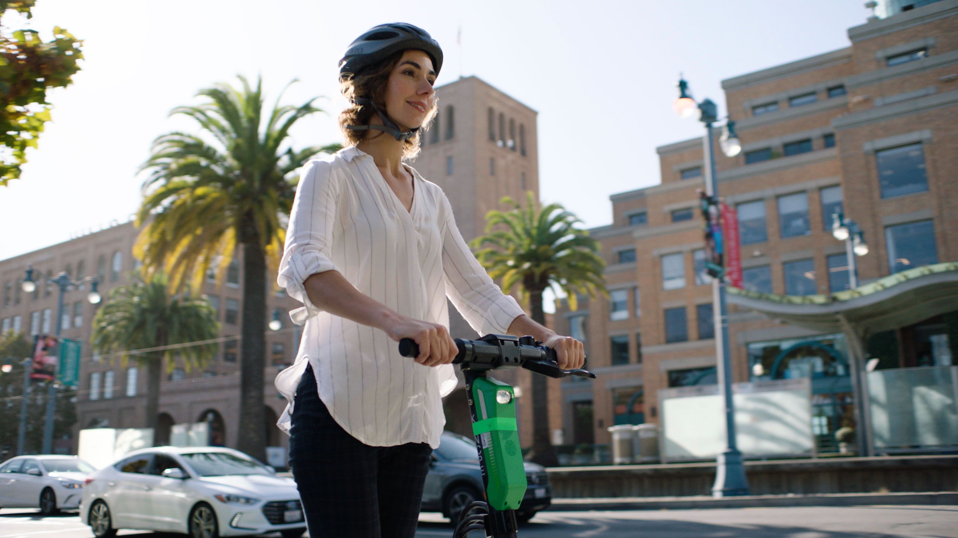 Junge Frau mit Helm auf dem Scooter unterwegs in der Stadt