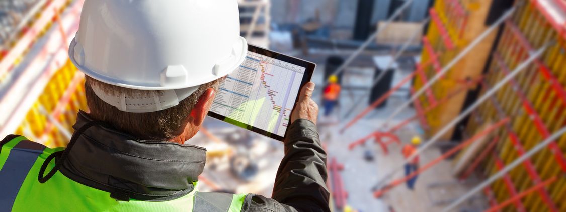 A worker is looking on a tablet screen at a construction site.