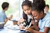 Focused African American and Asian schoolgirls help one another with their assignment in science class at a STEM elementary school.