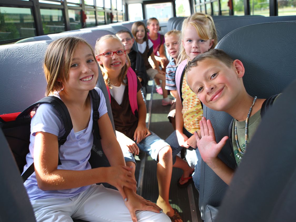 Students on a school bus smiling and waving