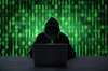 Person completely concealed in dark clothing hacking on laptop with green matrix background