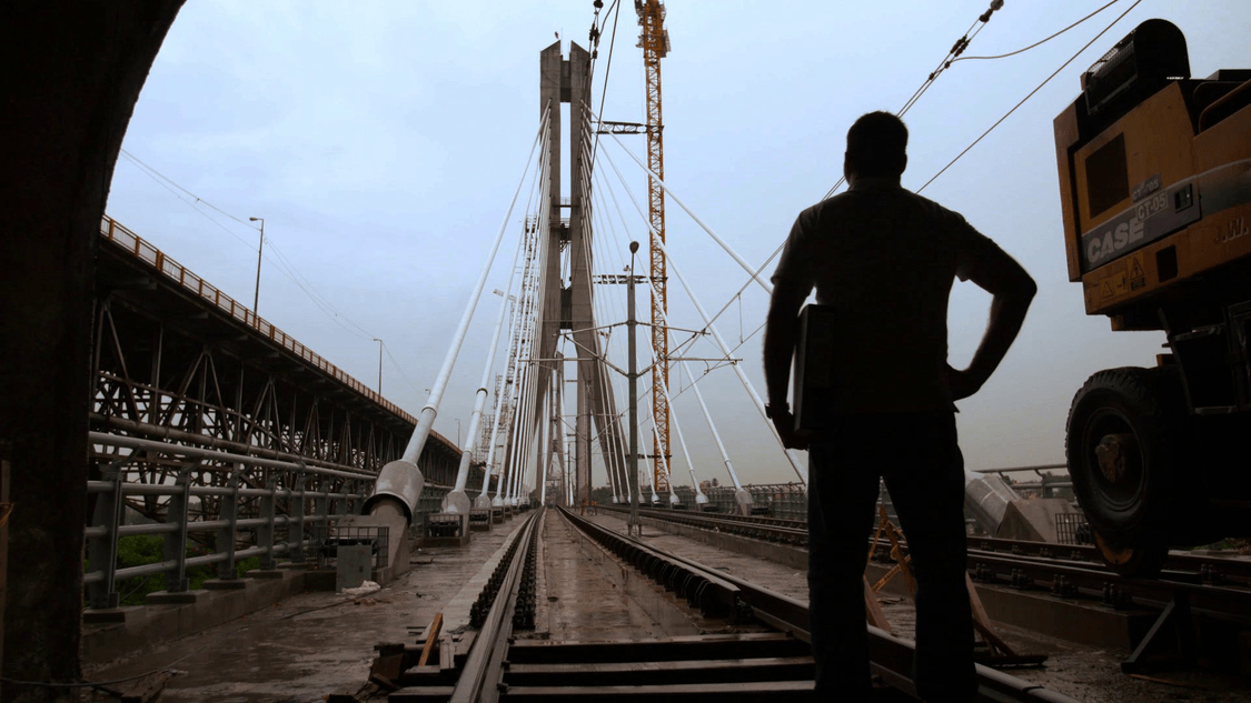 ein Mann vor einer Bahnbrücke blickt auf die Installationsarbeiten