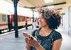 Woman curly hair is holding a smartphone an smiling while walking throu a railway station 