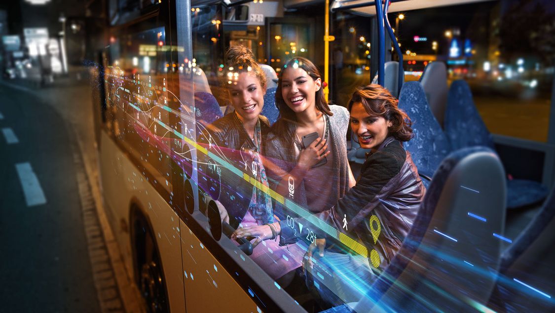Tři mladě vypadající ženy sedí v noci v autobuse, scéna je překryta digitálními grafickými prvky, které představují plynulou mobilitu