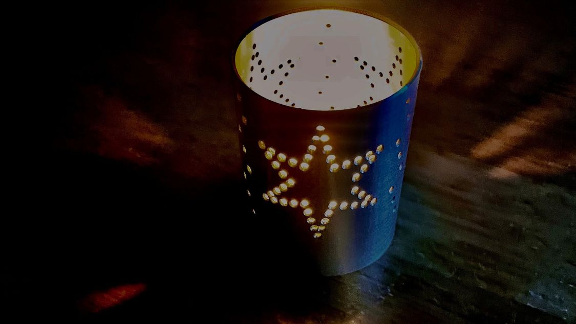 Photo: tealight holder "Star cup 2022", the candle is burning, light pattern on the table. 