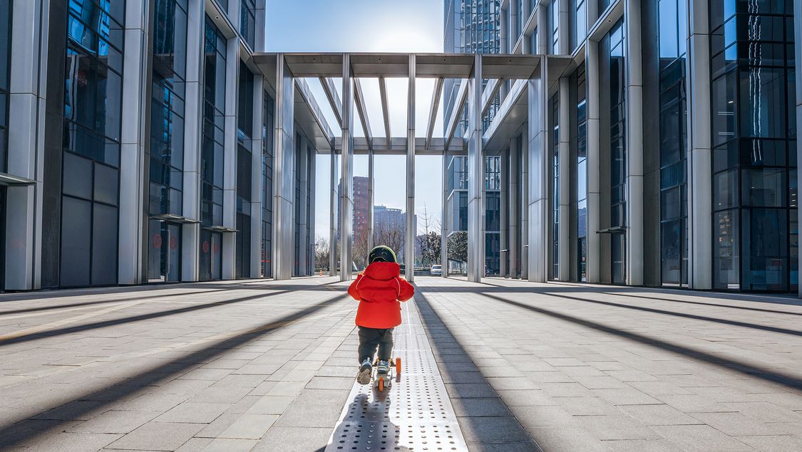 Kid on kickboard on a street between smart buildings