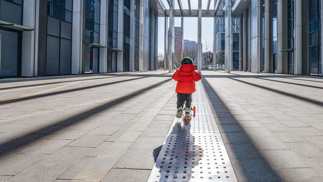 A 3-year-old kid is having fun on a scooter in modern city.