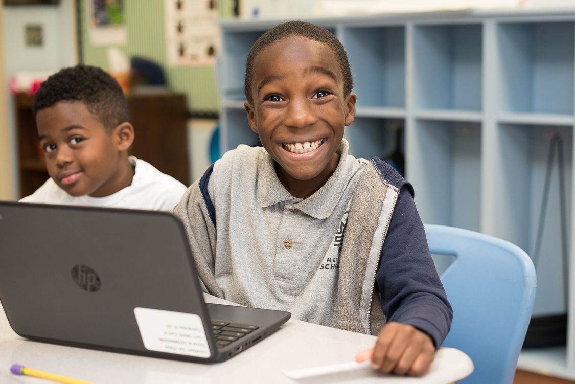 Boy sitting at desk in front of labtop with huge smile on face