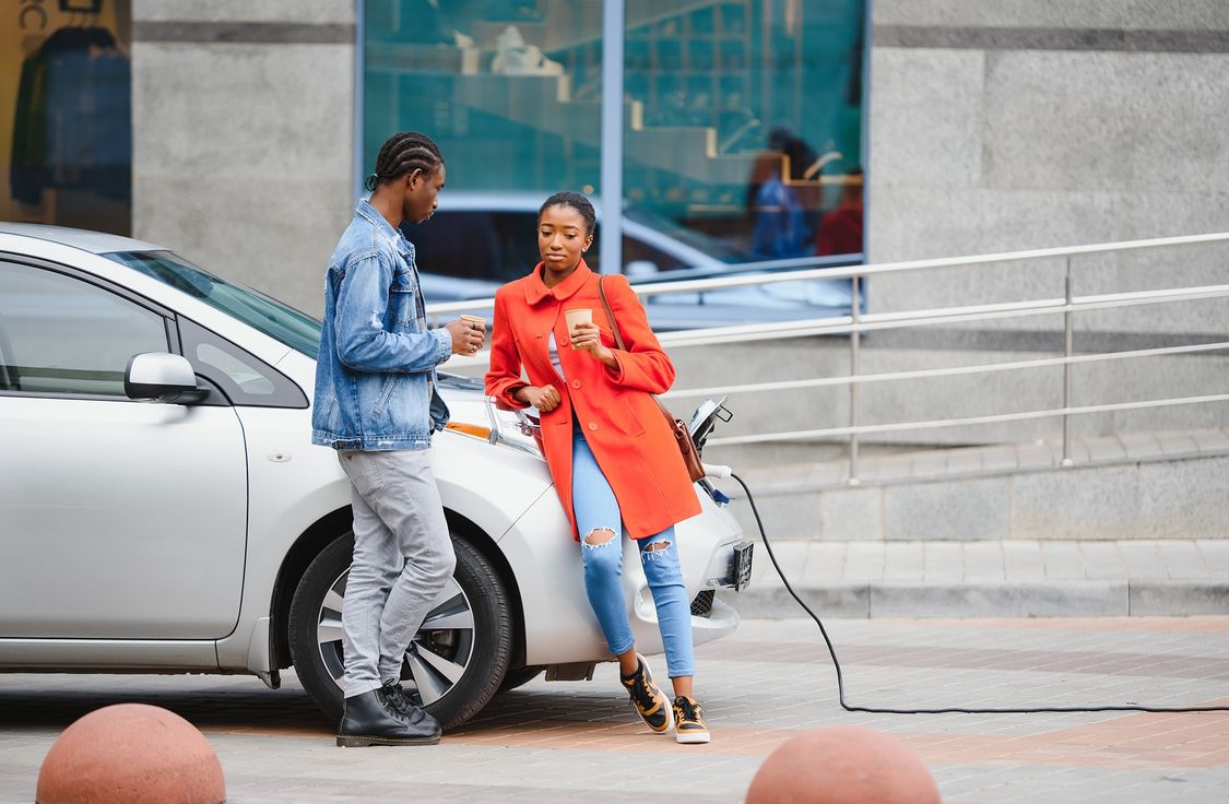 Happy young adult african american man and smiling woman charging electric car.