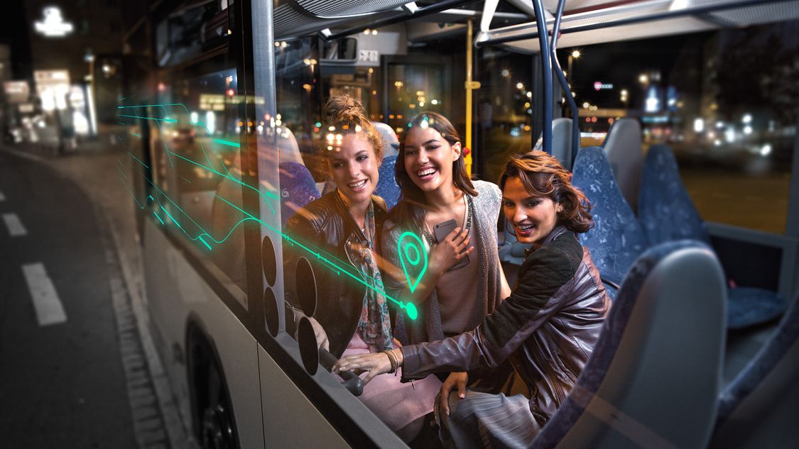 Three happy women on a bus at night looking out of the window