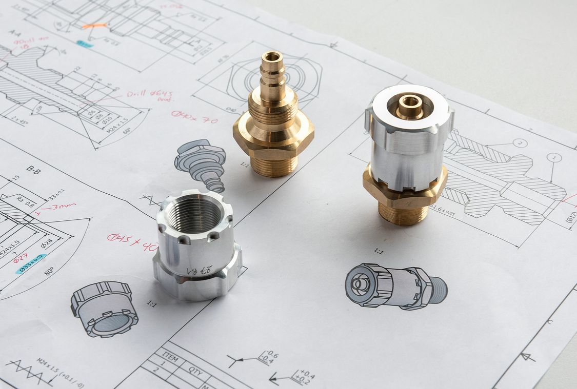 Photo: drawing of workpieces from the competition, placed on them the corresponding real workpieces (various complex turned parts, e.g. Gardena-style hose connectors).