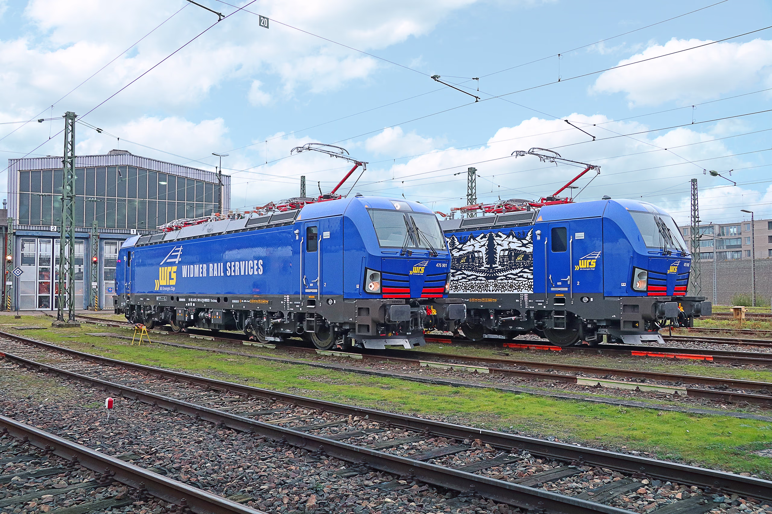 Two Vectron locomotives with battery power modules on rails in front of a hall. Siemens Mobility Vectron Battery Power Module