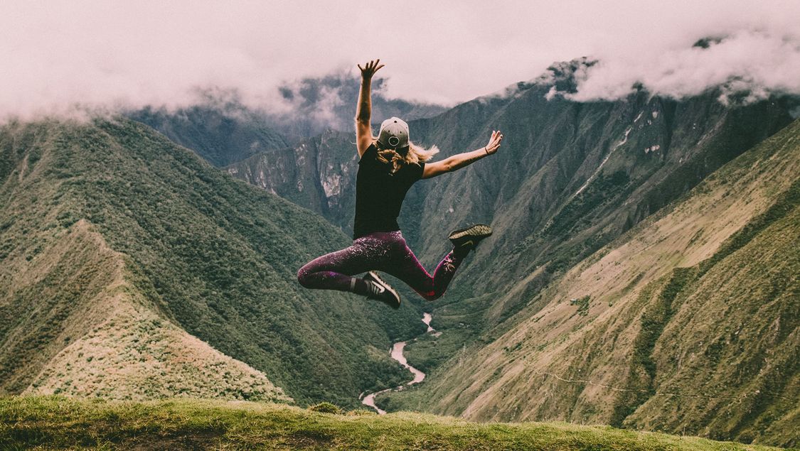 tjej hoppar glatt vid en grönskande bergstopp