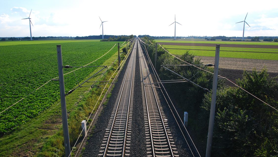 Two railtracks crossing rural landsape with wind tourbines in the horizont