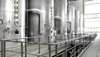 View on a plant section with a few large tanks within a plant of the sugar industry. In front of one tank a man in working clothes is standing and checking the setting.