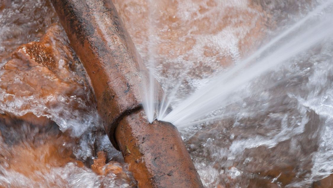 Picture of an old water pipe leaking, with water spraying out at high pressure