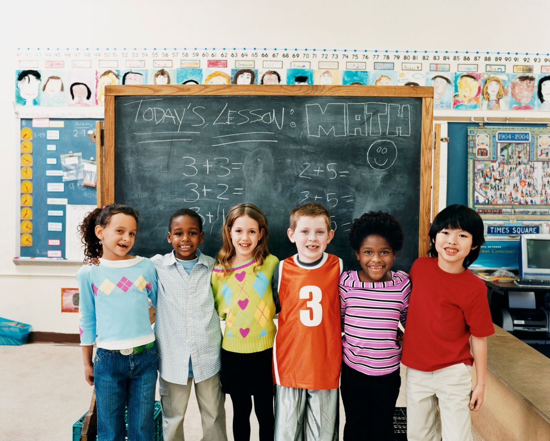 A group of smiling students stand in front of a chalkboard